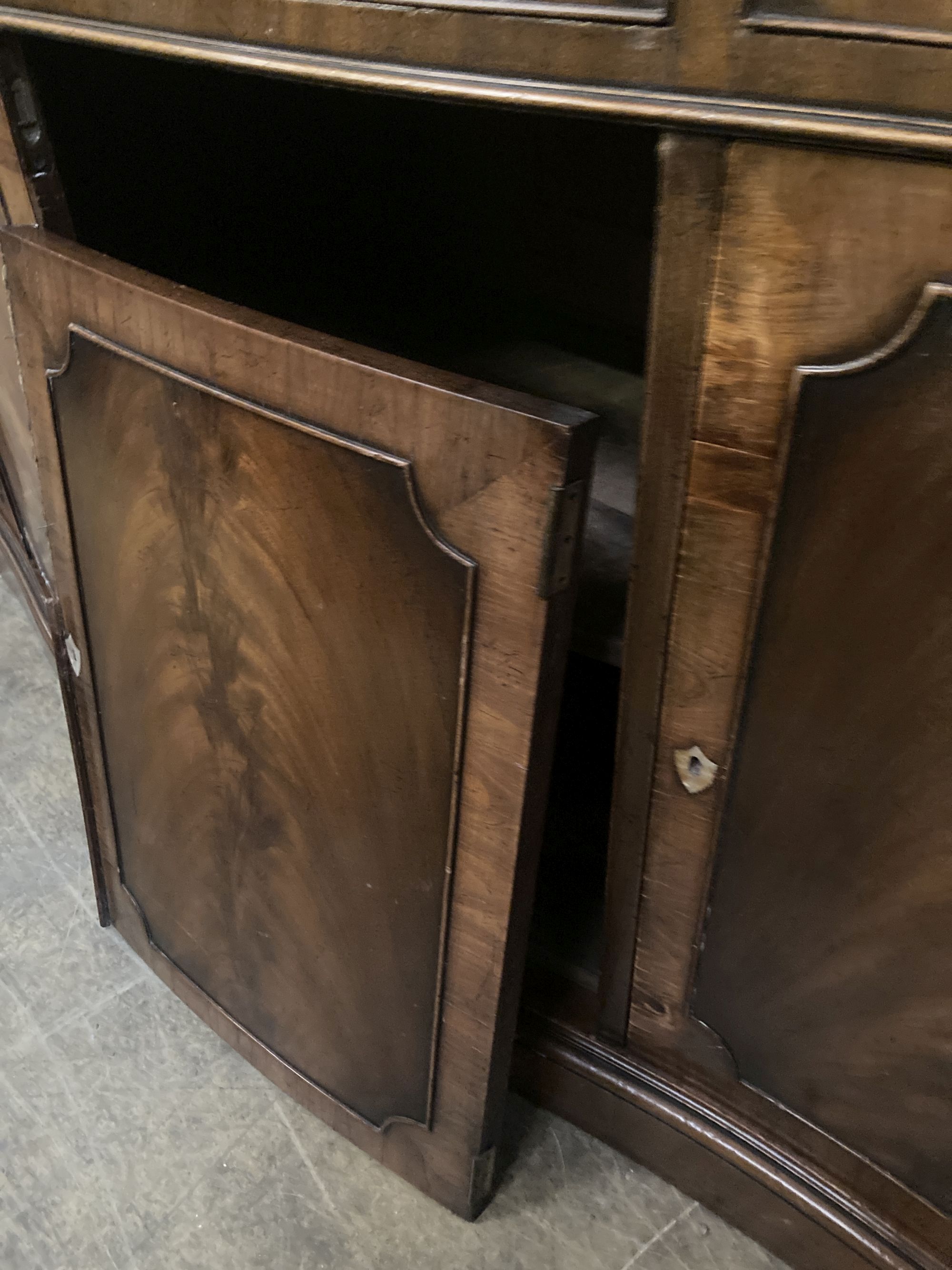 A George III style mahogany and walnut banded breakfront bookcase, with pierced broken swan neck pediment over oval glazing bars,